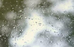 una foto de gotas de lluvia en el cristal de la ventana con una vista borrosa de los árboles verdes florecientes. imagen abstracta que muestra las condiciones meteorológicas nubladas y lluviosas