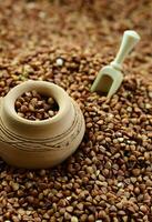 Background image of a large pile of buckwheat, in the middle of which lies a small jug and a wooden spatula for cereals photo