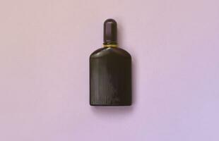 Dark purple perfume bottle with golden ribbon on pastel paper background. Trendy fragrance photo