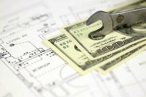 Spanner on top of money with blueprints of residential house plan. Restoring, repair, service maintenance cost photo