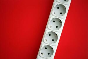 White electrical multi plug extender with european socket on bright red background photo