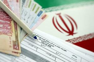 Iranian annual income tax return form F20-25-006 ready to fill on table with pen and iranian money on flag photo