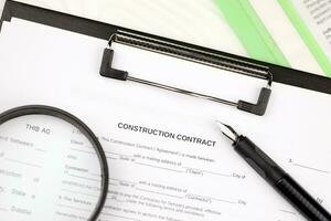 Construction contract form on A4 tablet lies on office table with pen and magnifying glass photo