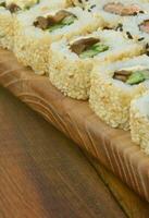 Close-up of a lot of sushi rolls with different fillings lie on a wooden surface. Macro shot of cooked classic Japanese food with a copy space photo