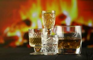 Different alcohol drinks in glass on wooden surface on fireplace background. Luxury elite alcohol in glass cups. Low key scene photo