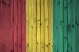 Guinea bandera representado en brillante pintar colores en antiguo de madera pared. texturizado bandera en áspero antecedentes foto