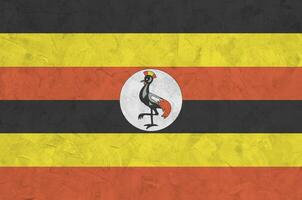 Uganda flag depicted in bright paint colors on old relief plastering wall. Textured banner on rough background photo