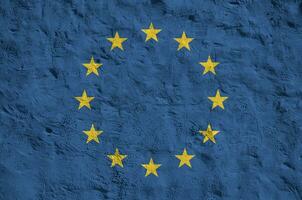 European union flag depicted in bright paint colors on old relief plastering wall. Textured banner on rough background photo