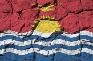 Kiribati flag depicted in paint colors on old stone wall closeup. Textured banner on rock wall background photo