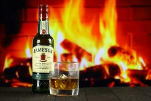 KYIV, UKRAINE - MAY 4, 2022 Jameson original alcohol bottle on wooden table with red fireplace photo