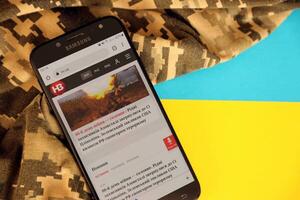 KYIV, UKRAINE - 4 MAY, 2023 NV ukrainian news portal on smartphone screen with ukrainian flag and camouflage fabric photo