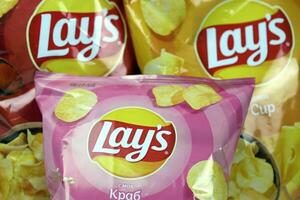 KHARKOV, UKRAINE - JANUARY 3, 2021 Various flavoured of lay's potato chips on wooden background. Lay's has been owned by PepsiCo through Frito-Lay in 1965 photo