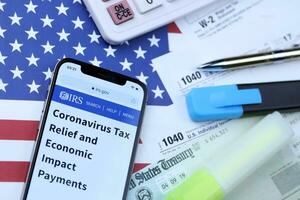 KHARKOV, UKRAINE - MARCH 5, 2021 Official IRS website on iPhone 12 pro screen with 1040 and w-2 paper tax forms on US flag photo