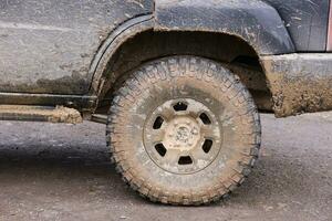 Wheel closeup in a countryside landscape with a mud road. Off-road 4x4 suv automobile with ditry body after drive in muddy road photo