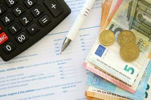 Filling french tax form process with calculator, pen and euro money bills close up. Tax paying period photo