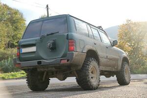 Automobile in a countryside landscape with a mud road. Off-road 4x4 suv automobile with ditry body after drive in muddy road photo