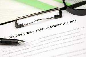 Drug and alcohol testing consent form on A4 tablet lies on office table with pen and magnifying glass photo