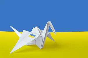 Ukraine flag depicted on paper origami crane wing. Handmade arts concept photo