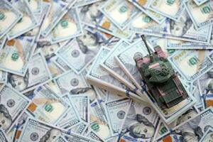 Toy tank on US hundred dollar bills banknotes. The concept of war costs, military spending and economic crisis photo