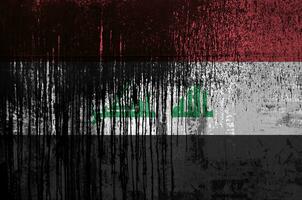 Iraq flag depicted in paint colors on old and dirty oil barrel wall closeup. Textured banner on rough background photo