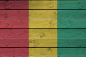 Guinea bandera representado en brillante pintar colores en antiguo de madera pared. texturizado bandera en áspero antecedentes foto
