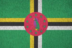 Dominica flag depicted in bright paint colors on old relief plastering wall. Textured banner on rough background photo