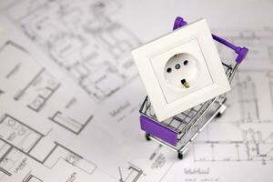 European standard EU outlet in small shopping cart on blueprints of residential house plan. Concept of shopping and electricity devices photo