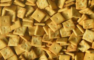A lot of small cookies are square shaped. A pattern of a yellow salt cracker. Background image with salted pastry photo