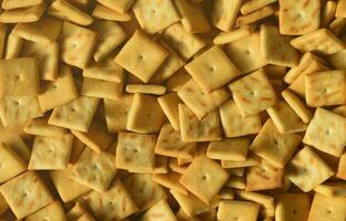 A lot of small cookies are square shaped. A pattern of a yellow salt cracker. Background image with salted pastry photo