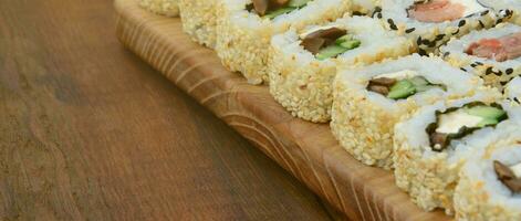 el primer plano de muchos rollos de sushi con diferentes rellenos se encuentra sobre una superficie de madera. foto macro de comida japonesa clásica cocinada con un espacio de copia