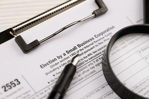 IRS Form 2553 Election by a Small Business Corporation tax blank on A4 tablet lies on office table with pen and magnifying glass photo