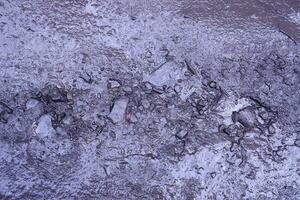 Close up of muddy puddle with small stones on wet surface. Background texture with top view photo