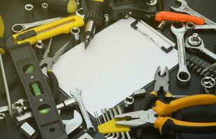 Handyman tool kit on black wooden table with copy space in blank paper tablet. Many wrenches and screwdrivers, pilers and other tools for any types of repair or construction works photo