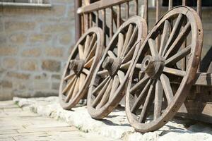 Three old wooden wheels for horse carts leaning against a wooden wall photo