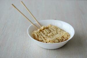 Bowl of instant cooking noodles with wooden chopsticks on white wooden table photo