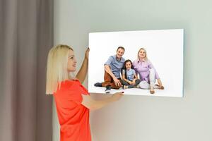 A happy young blonde woman is holding a large wall photo canvas at home