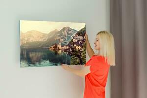 A happy young blonde woman is holding a large wall photo canvas at home