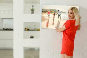 un contento joven rubia mujer es participación un grande pared lona a hogar foto
