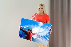 un contento joven rubia mujer es participación un grande pared foto lona a hogar