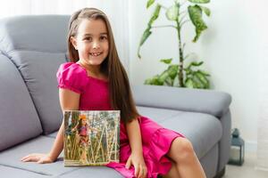 Cute little girl holding photo canvas at home