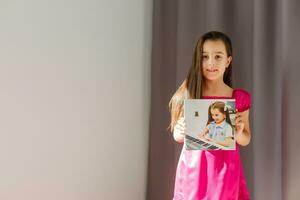 Cute little girl holding photo canvas at home