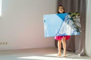 Cute little girl holding photo canvas at home