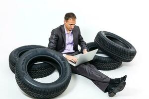 A serious businessman sitting on a stack of car tires. Repair shop. Car service. Spare parts reselling. solated on white background photo