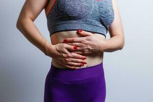 Beautiful girl in sportswear is touching her stomach feeling pain, on gray background photo