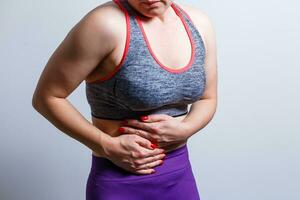 Beautiful girl in sportswear is touching her stomach feeling pain, on gray background photo