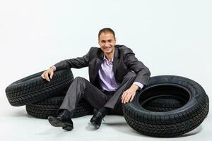 Full length portrait of a young businessman leaning on a pile of car tires isolated on white background photo