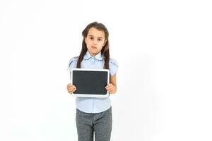 hermosa colegio niña en un negocio traje participación un tableta en su manos y mirando dentro el cámara, selectivo atención en el tableta foto