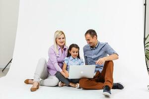 Happy family lying down on the floor while surfing on internet online with laptop, isolated over white photo