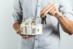 man in casual clothes posing isolated on white wall background. Holding in hands house and bunch of keys photo