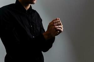 hombre guapo sentarse oración sobre fondo negro. sus manos están orando por las bendiciones de dios. foto